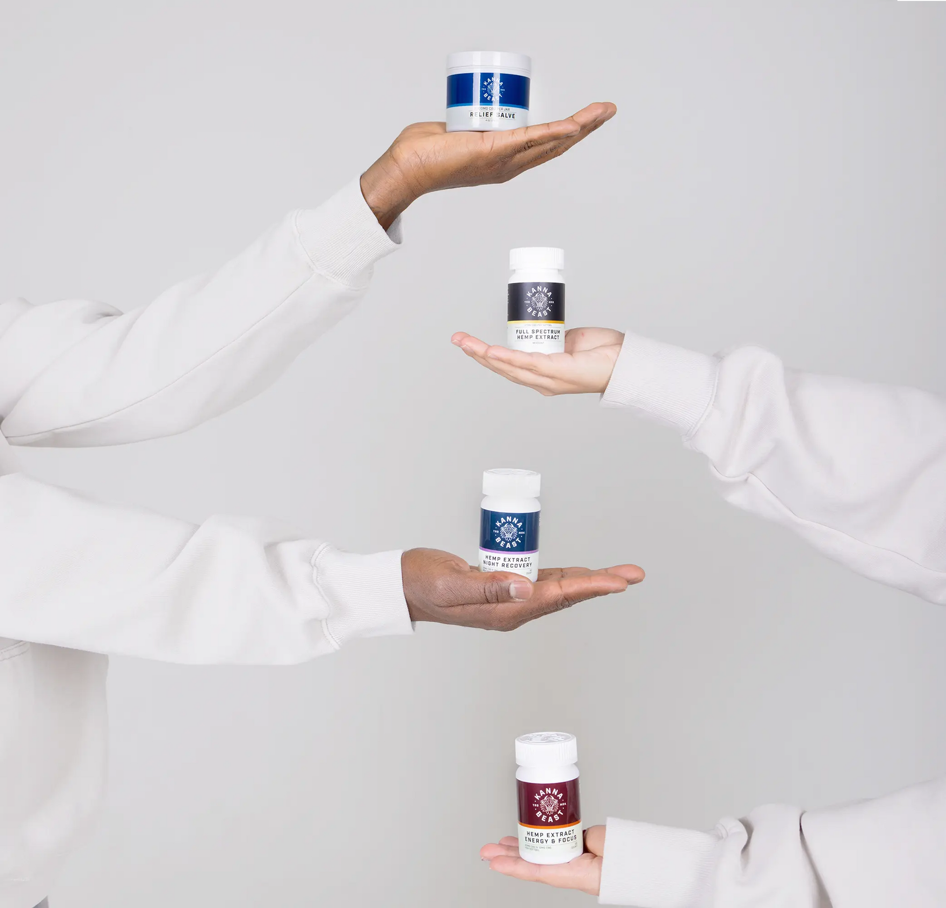 Hands holding Kanna Beast CBD Athletic Recovery Bundle products including Relief Salve, Full Spectrum Hemp Extract, Night Recovery, and Energy & Focus supplements against minimalist white background